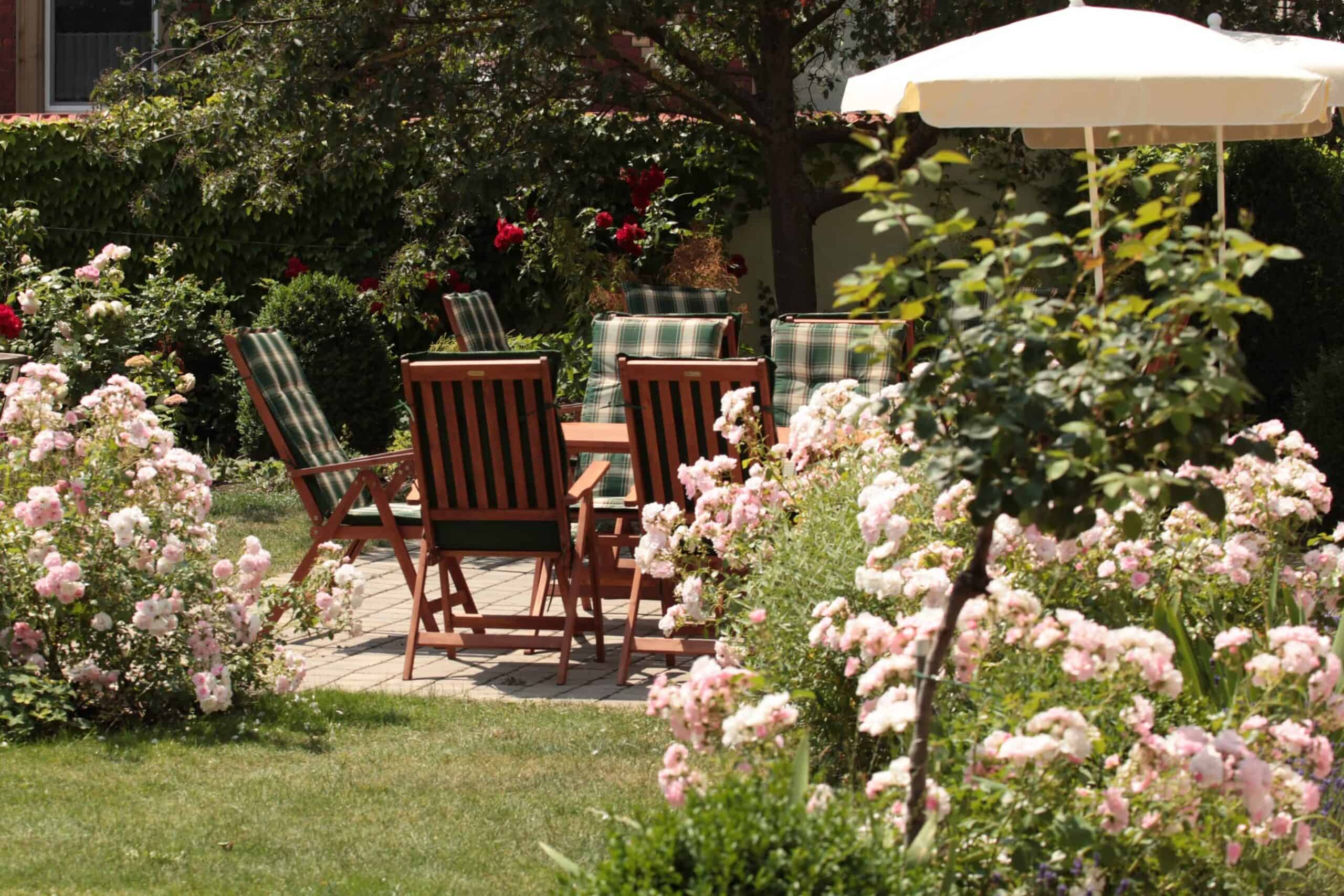 Gartentisch mit Stühlen ist umringt mit rosa und roten Rosen