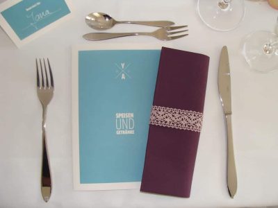 blaue Speisekarte und lila Serviette zwischen Essensbesteck
